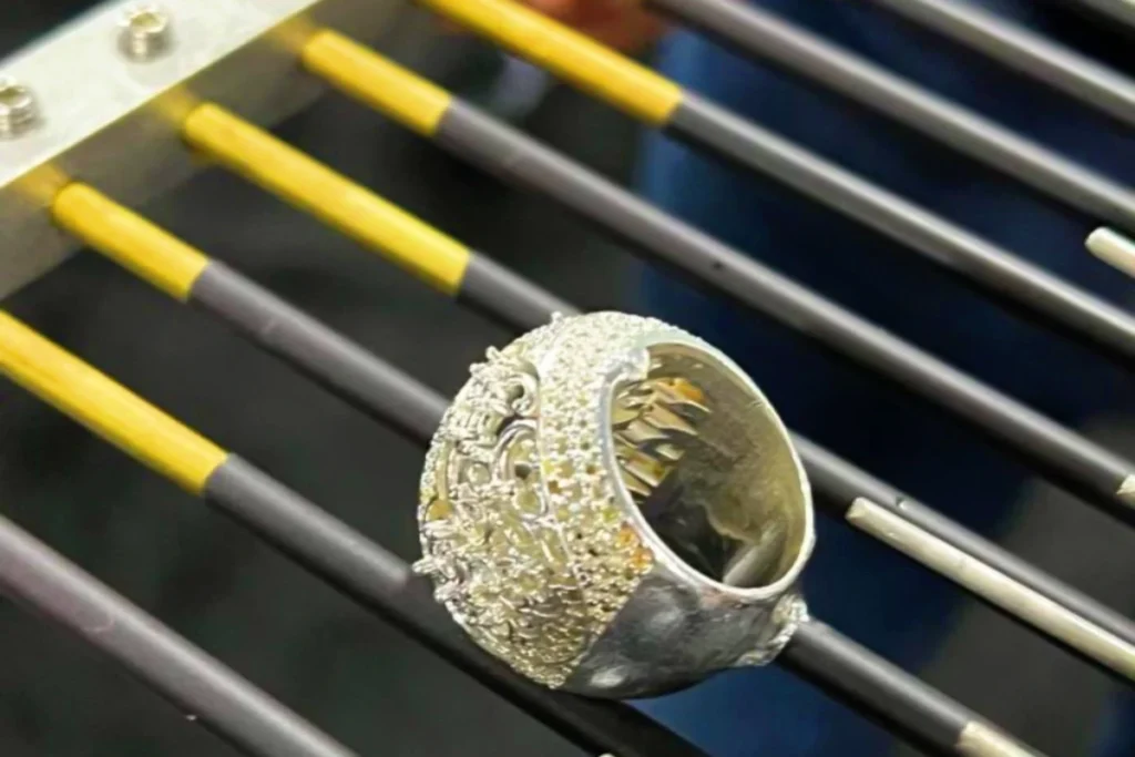 Success in jewelry making goes far beyond selecting premium materials and meticulous craftsmanship; what matters even more is the finish of the surface. This often-overlooked step plays a crucial role in the jewelry industry, as a flawless surface is not only an aesthetic choice but also a symbol of quality and craftsmanship.
Electrolytic polishing and hand polishing are currently the two most common techniques. Both enhance surface finish, but they differ significantly in principle, results, and applications. So, which method is better? The answer actually depends on your specific needs.
Understanding Electrolytic Polishing
Electrolytic polishing is a process that uses electrochemical methods to remove material from a metal surface, achieving a highly uniform polish even in hard-to-reach areas like beneath prong settings. It is particularly well-suited for handling intricate details and hard-to-reach areas, making it an ideal method for achieving exceptional surface quality.
This process is similar to “reverse electroplating,” where the outer layer or “skin” of a metal component is removed (electropolishing improves the jewelry’s surface by selectively dissolving the outermost layer of metal), thereby eliminating microscopic surface imperfections (such as small burrs and scratches). The result is a jewelry surface as smooth as a mirror! Because it allows for batch processing and is highly efficient, electrolytic polishing is widely used in medical devices, precision parts, and industrial manufacturing.
Understanding Hand Polishing Techniques
Hand polishing involves manual operation using rotary tools, such as micro-motors, flexible shafts, or polishing motors, as well as traditional hand tools. This method requires a high level of operator experience and relies heavily on technical skill, particularly for high-end surface finishing.
Although the level of precision may not match that of electrolytic polishing, the operator can adjust the technique according to specific needs to achieve a high-gloss or even mirror-like finish. It allows for localized treatment of specific areas. By creating different levels of luster and visual effects on various surfaces of a piece, it is better suited for decorative and artistic works. Therefore, in jewelry making, hand polishing remains an irreplaceable and crucial step.

Can electrolytic polishing completely replace manual polishing?
Many mechanical engravers often ask this question. However, the answer is clearly no—it cannot completely replace manual polishing.
While electrolytic polishing excels at improving surface smoothness and removing microscopic defects, it still has limitations in the following areas: it is difficult to achieve a true mirror-like high-gloss finish, it lacks the ability to perform precise localized control, and it lacks artistic expressiveness—all of which are precisely the strengths of manual polishing.
Practical Applications in the Industry
In actual production, these two processes are typically used in conjunction rather than as substitutes for one another. In a production setting, manual polishing faces significant challenges because it relies on skilled labor—a resource that may be scarce—and often results in inconsistent polishing outcomes. Different polishing technicians often prefer different polishing wheels and compounds, leading to variations in surface finish among workpieces completed by different workers, and the risk of over-polishing exacerbates this issue. The appropriate use of electrolytic polishing can effectively address these manual challenges and improve efficiency. The common process is as follows:
Step 1: Precise Material Removal
The electrolytic polishing process effectively smooths metal surfaces while preserving fine details and maintaining the original design and geometry, preventing any rounding or deformation of edges.
Step 2: Ensuring Consistent Results for Every Product
Precise control of material removal using an electrolytic polishing machine ensures surface finish and quality for every piece of jewelry. This high level of consistency is crucial for maintaining brand reputation and meeting customer expectations.
Step 3: Enhancing Luster
While machine-polished surfaces are precise and uniform, they often lack luster. Manual re-polishing with sandpaper or polishing paste is therefore necessary. Designs requiring special attention may undergo multiple polishing passes to achieve a multi-layered luster effect.
Step 4: Refining Details to Enhance Texture
A key factor in attracting consumers to jewelry pieces is their unique texture. To ensure each product exhibits a distinctive texture, designers are given creative freedom to refine details according to their vision. By manually creating varied light reflections in specific areas (using rollers or other hand-polishing tools), they ultimately achieve a unique tactile quality.
Step 5: Precious Metal Recovery
Since the metal removed from the surface during the electrolytic polishing process is collected on the cathode, precious metal recovery becomes much simpler! The cathode collects pure metal, which is a significant advantage compared to the situation where metal particles in dust collector bags are mixed with abrasive and polishing agent debris.


If you ask any jeweler what they enjoy doing most on their pieces, how many would say polishing?! This combination ensures both efficiency and the final result. It makes the combination of electrolytic polishing and hand polishing an extremely attractive method for achieving high-quality surface finishes, suitable for hard-to-reach areas and allowing the operator to apply their own creative touch to specific sections, thereby enhancing the overall quality of the piece.
Discover Katway’s Electrolytic Polishing Machines
Polishing technology offers you the opportunity to adopt modern processes like electrolytic polishing while incorporating manual techniques, effectively elevating the standard of your jewelry and giving you—the jeweler—a competitive edge. Most conventional polishing machines are bulky and ill-suited for engravers. To enable engraving enthusiasts, small jewelers, and small workshops to achieve the perfect combination of electrolytic polishing and manual polishing, Katway has introduced an ultra-convenient flexible-shaft suspended motor for jewelry making. With a maximum speed of 20,000 RPM, it delivers the speed and efficiency required for precision jewelry tasks such as polishing, grinding, and engraving. The flexible-shaft design ensures ease of operation and allows for effortless access to complex areas, making it an ideal choice for the fine finishing of small, delicate jewelry pieces such as rings, pendants, and bracelets.

Summary
Electrolytic polishing and hand polishing are not mutually exclusive; rather, they are complementary. If you prioritize efficiency, electrolytic polishing is the way to go; if you prioritize texture and detail, hand polishing remains indispensable. In modern manufacturing and the jewelry industry, combining the two is the most mature and efficient solution.